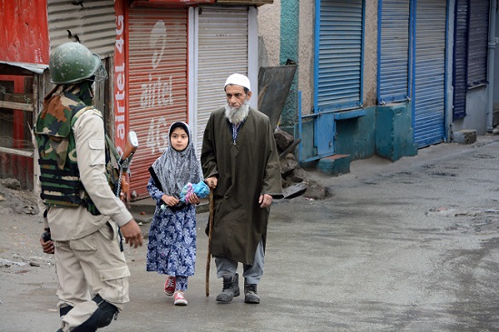 An elderly man and his granddaughter walk past a security personnel during the curfew imposed after killing of terrorist Zakir Musa in Srinagar on May 24, 2019. (Photo: PTI)