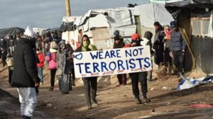 Refugees in France hold a placard that says “we are not terrorists” during the dismantling of their refugee camp in February 2016. (File Photo: AFP)